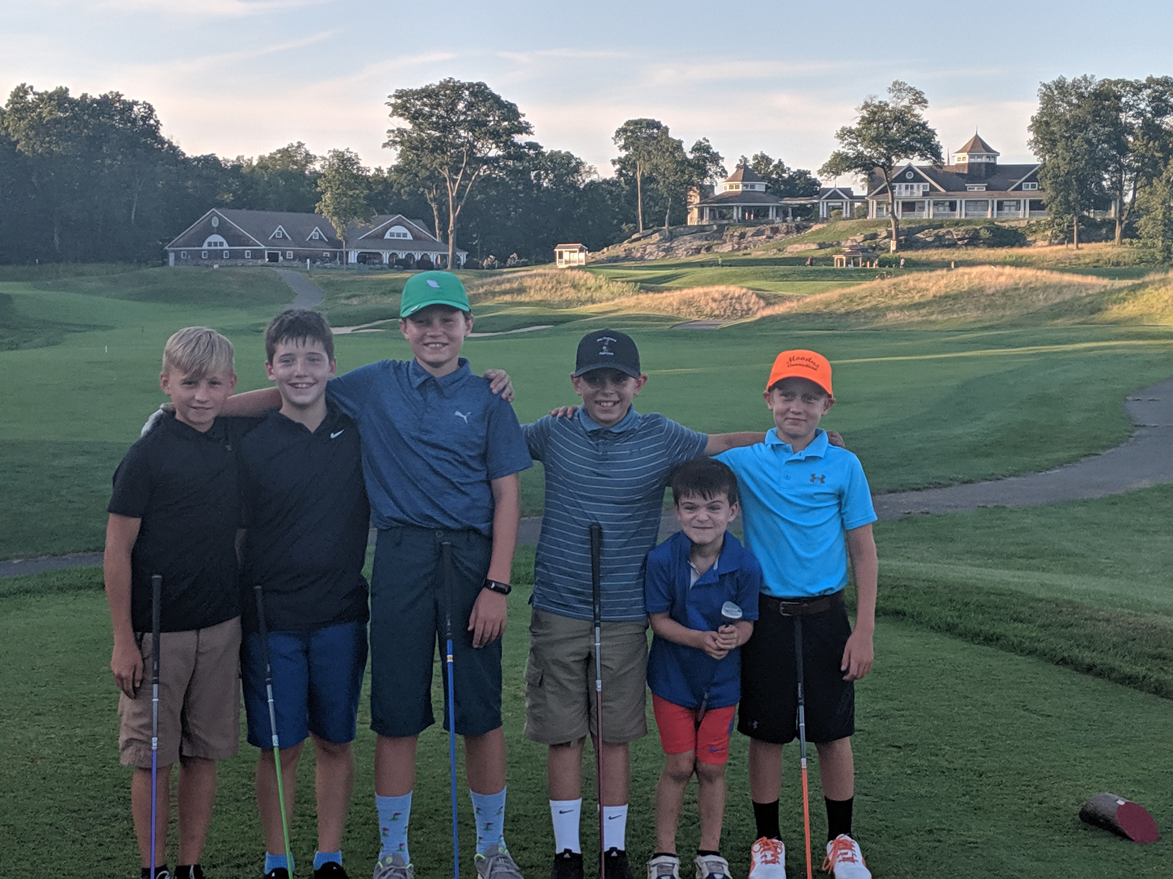 5 boys standing on 9th hole with clubhouse in background